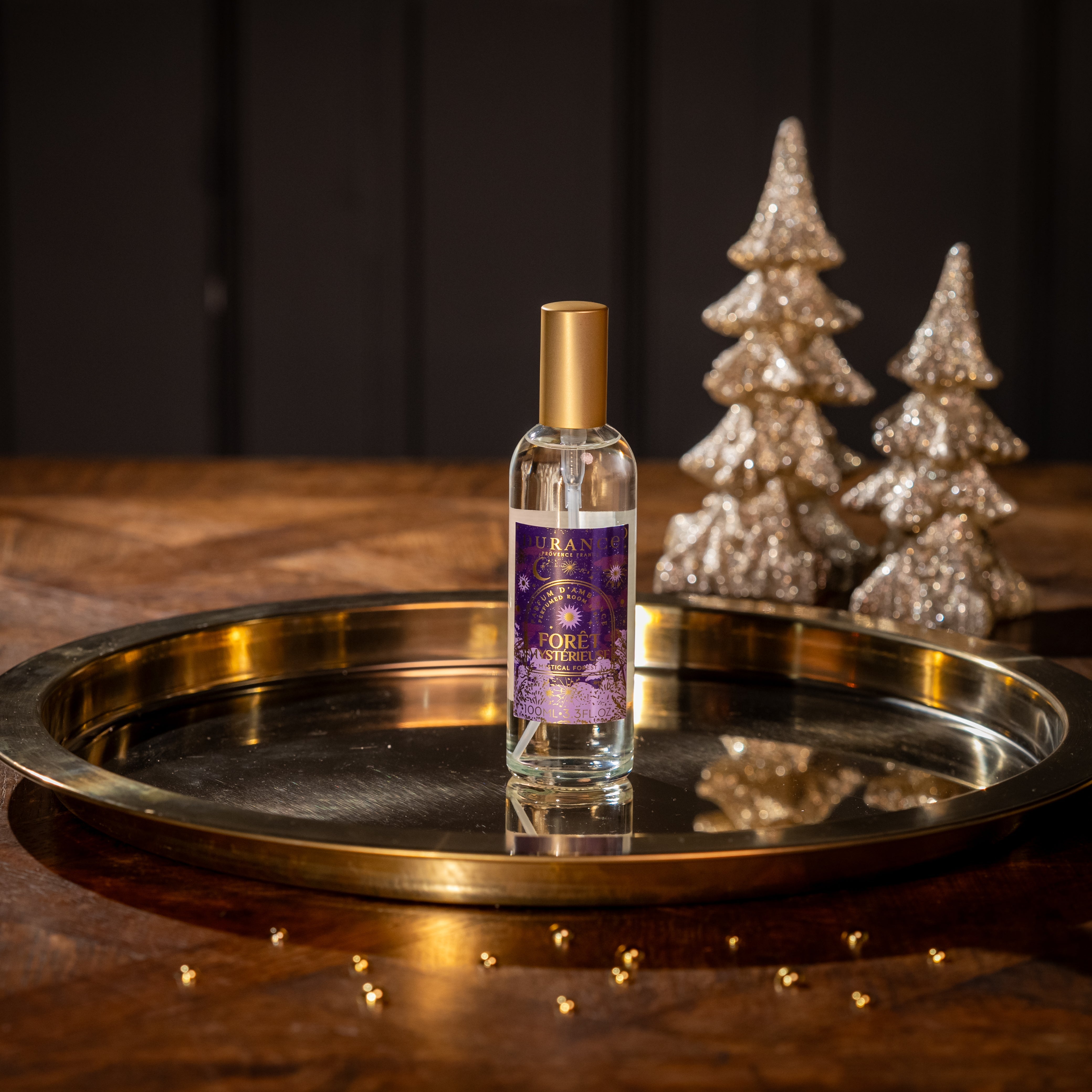 Bottle of Room Spray on a gold tray with decorative trees in the background