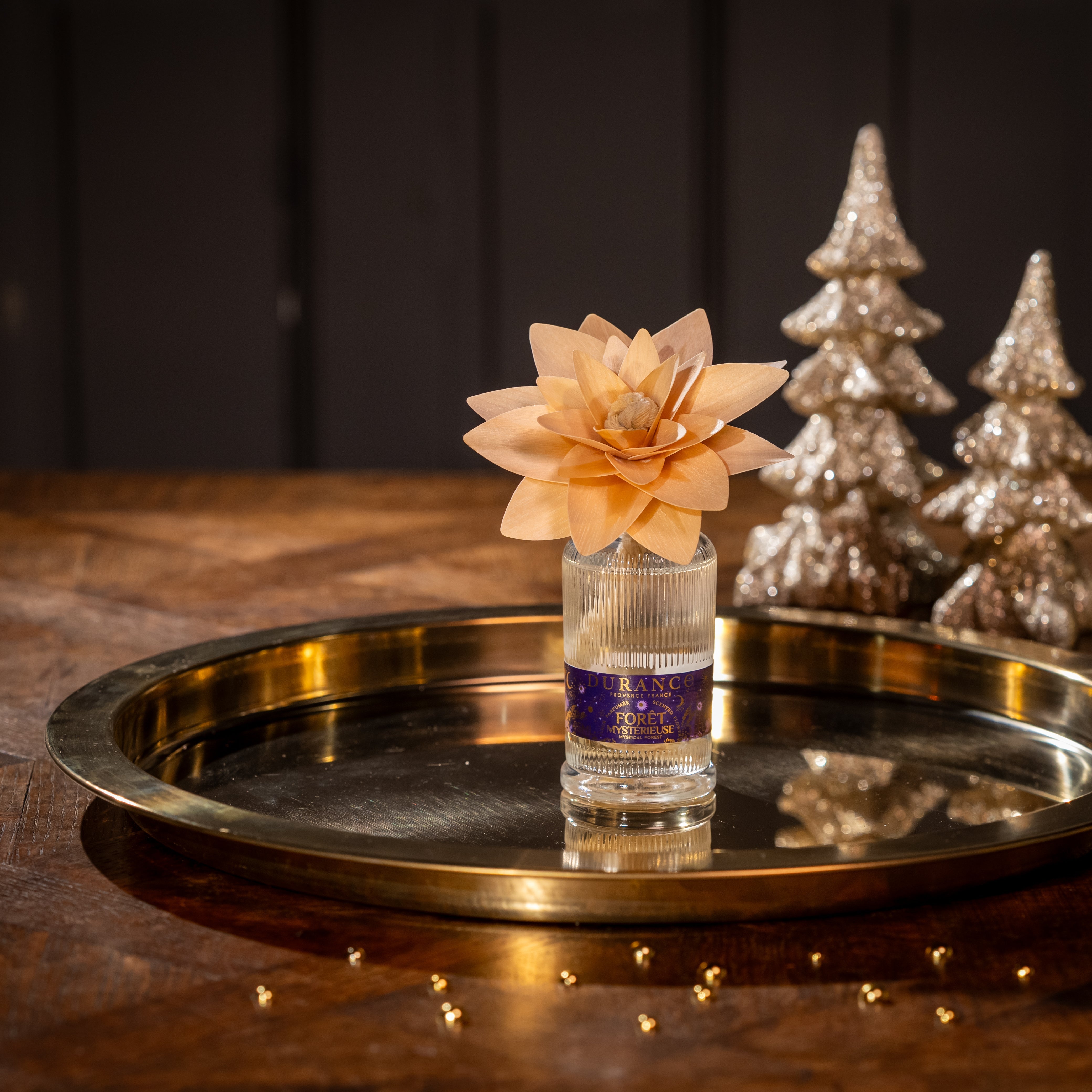 Small bottle of alcohol with a decorative flower on a metallic tray, with decorative trees in the background.