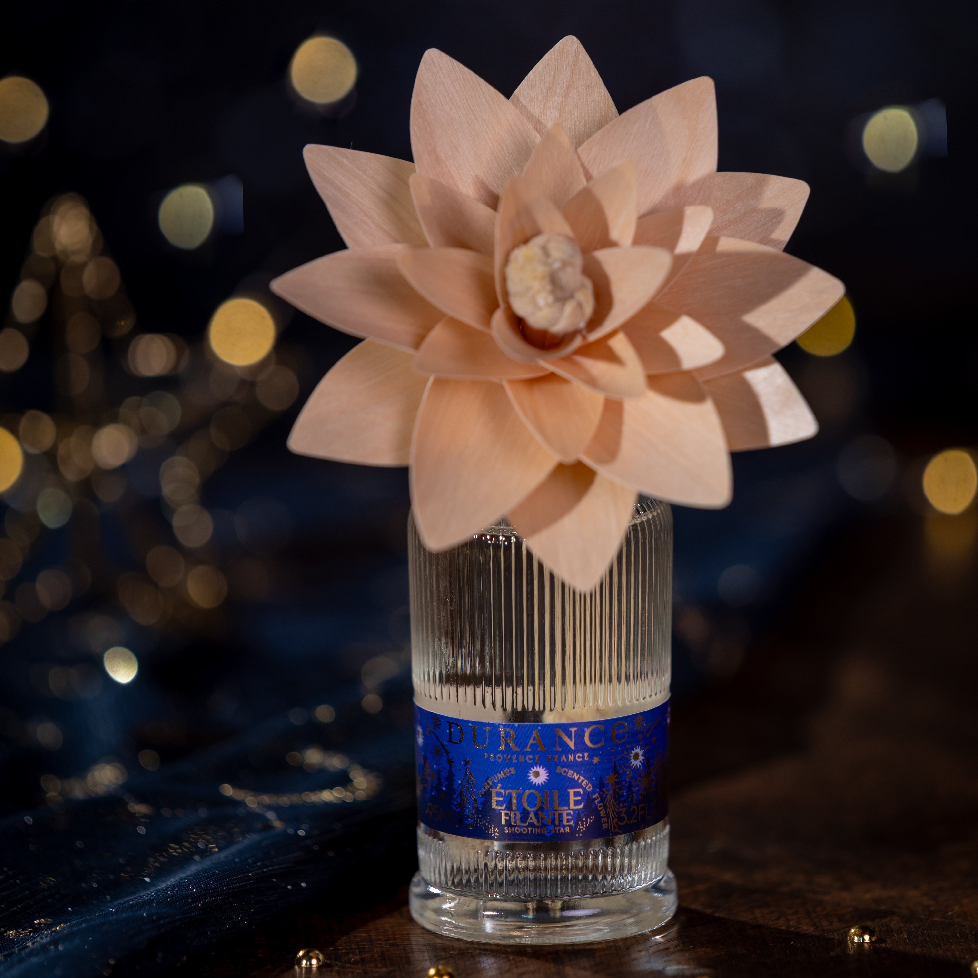 Decorative flower in a glass vase with a blue label against a dark background with lights.
