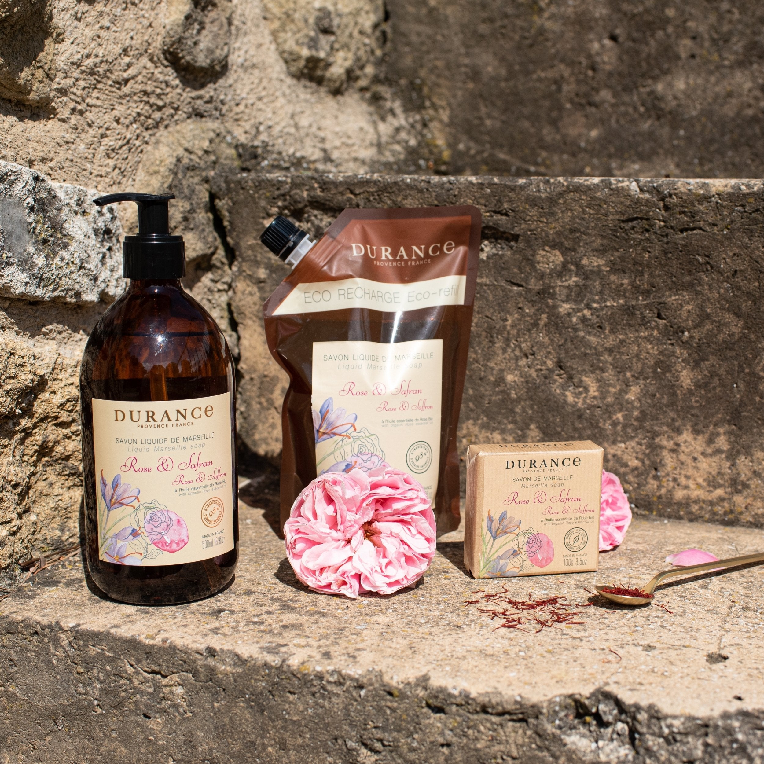 Durance skincare products including a bottle, pouch, soap, and pink flower on stone steps.
