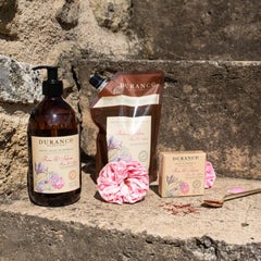 Durance skincare products including a bottle, pouch, soap, and pink flower on stone steps.