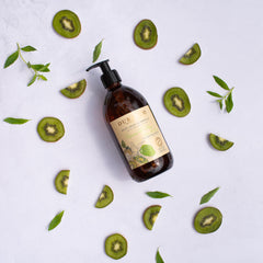 Brown bottle with a label on a white background surrounded by sliced kiwis and leaves