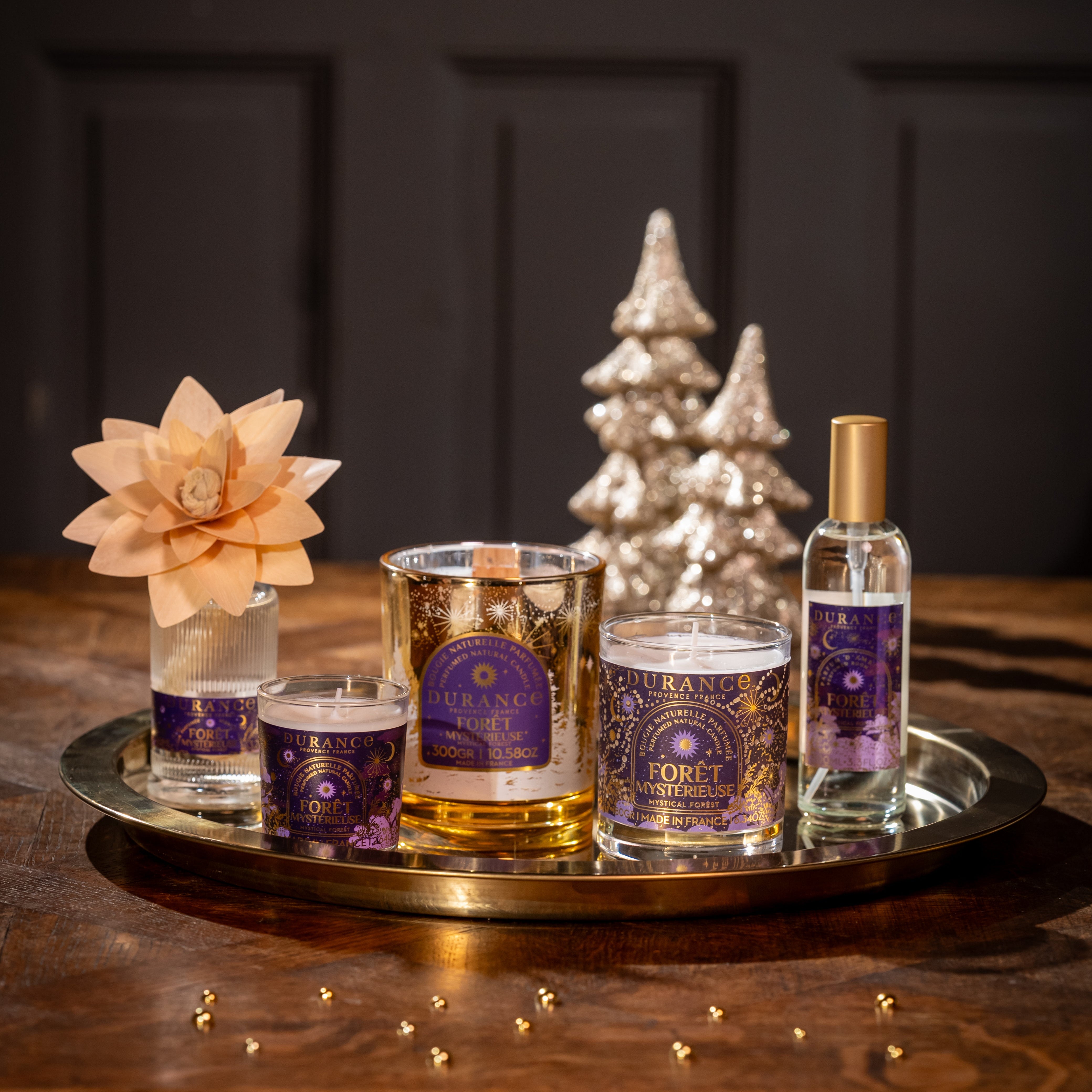 Tray with candles, a small tree, and decorative items on a wooden surface with a dark background.
