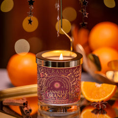 Candle labeled 'Cannelle Orange' with star-shaped earrings on a decorative tray with oranges and cinnamon sticks.