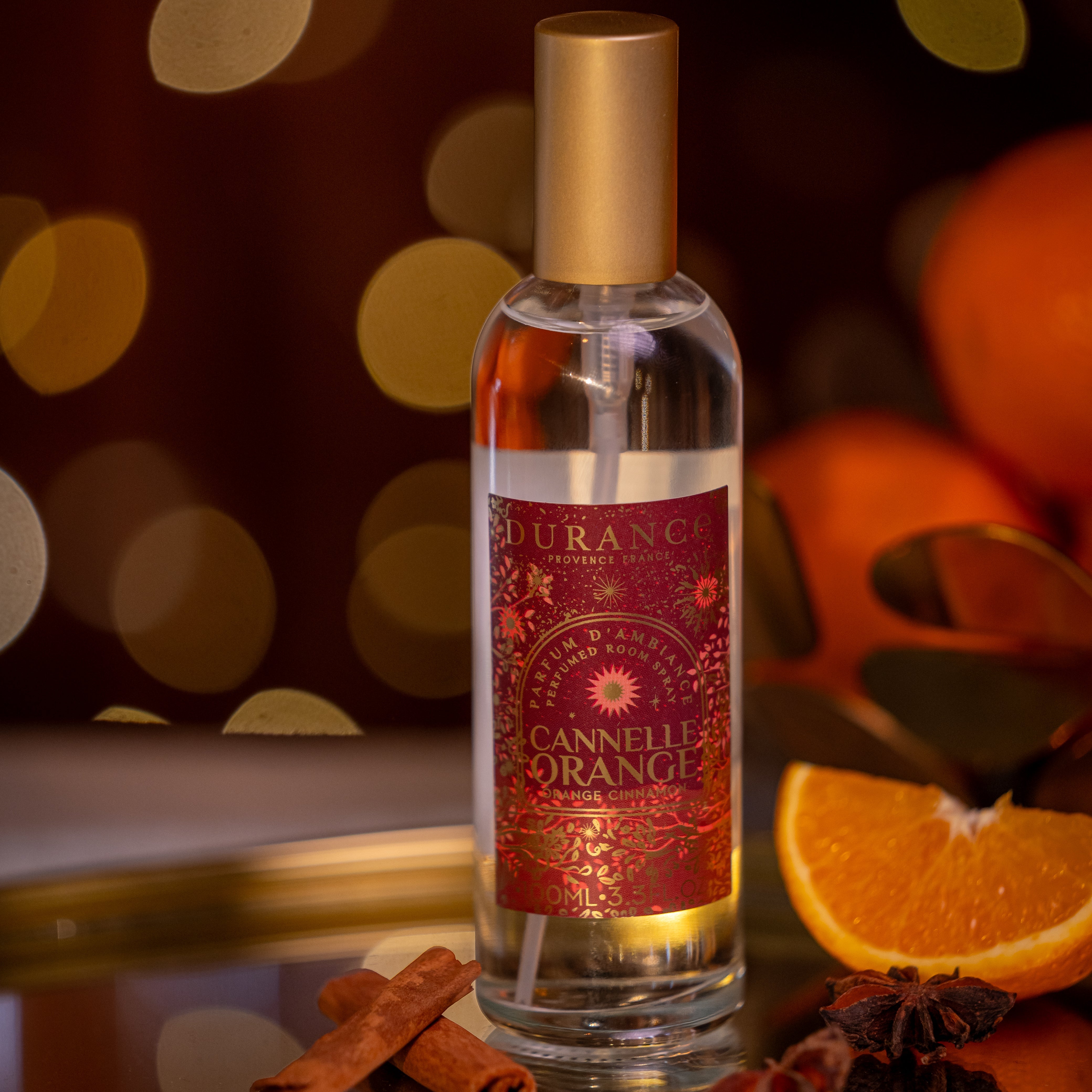 Bottle of Durance Cannelle Orange on a decorative tray with oranges and cinnamon sticks against a bokeh background.