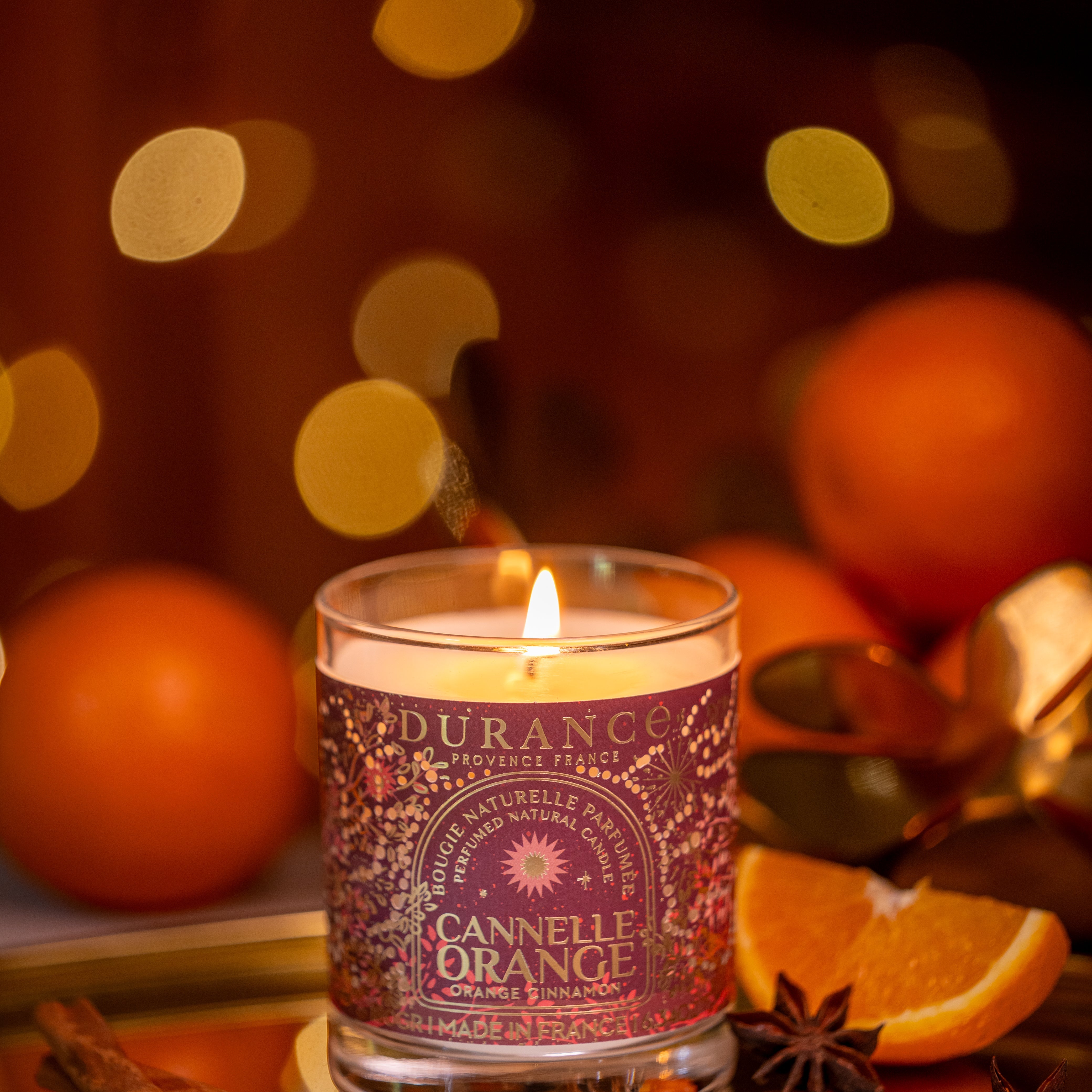 Candle labeled 'Durance Cannelle Orange' with oranges and spices on a blurred background