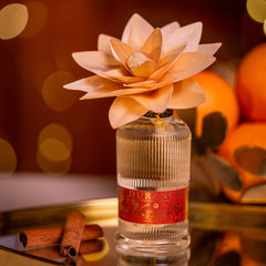 Perfume bottle with a decorative flower on top against a warm, blurred background