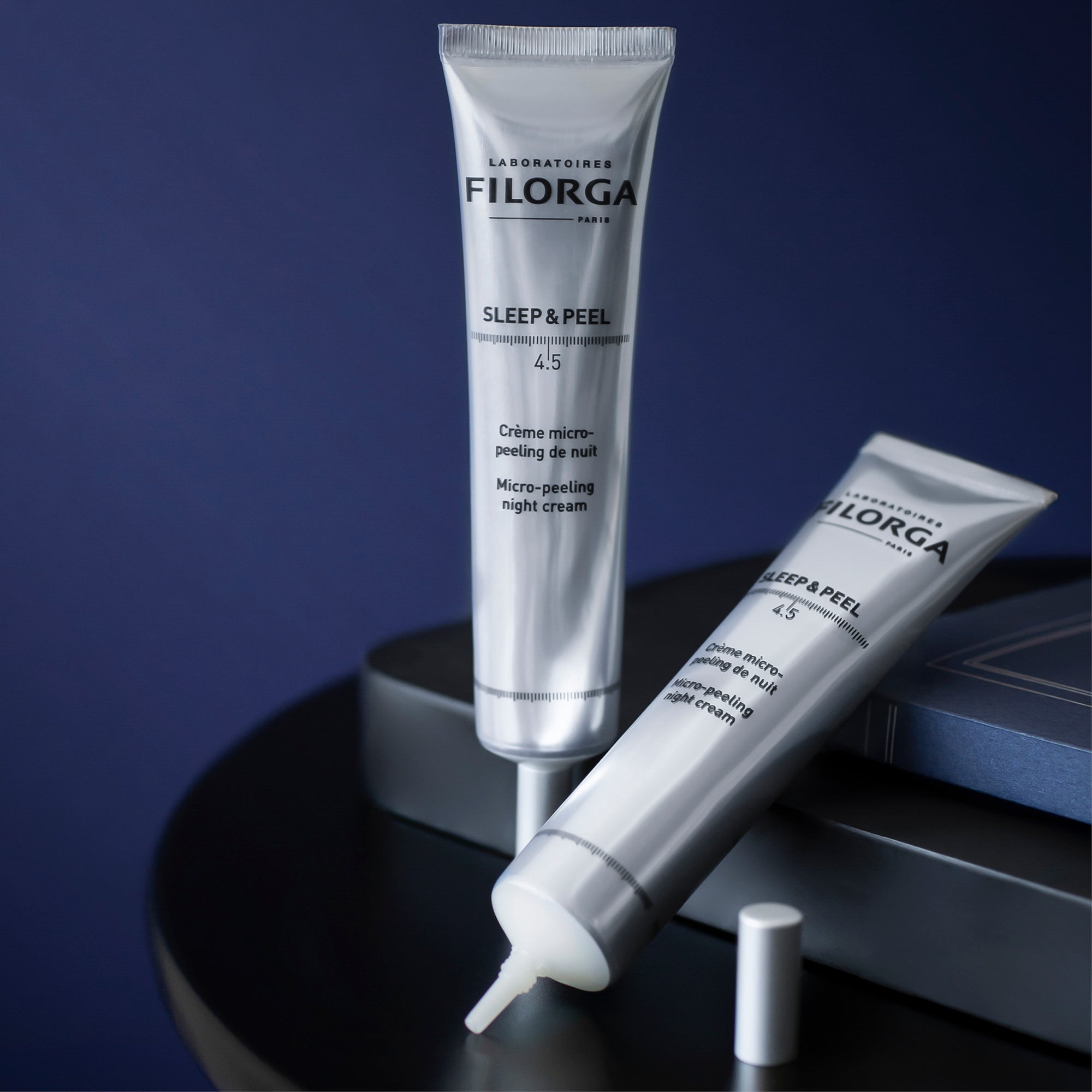 Two tubes of Filorga Sleep & Peel cream on a dark surface with a blue background