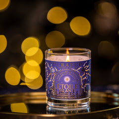 Candle in a glass container with a blue label on a dark background with blurred lights