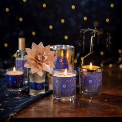 Decorative candles with blue glass holders on a wooden surface against a dark background with star-like lights.