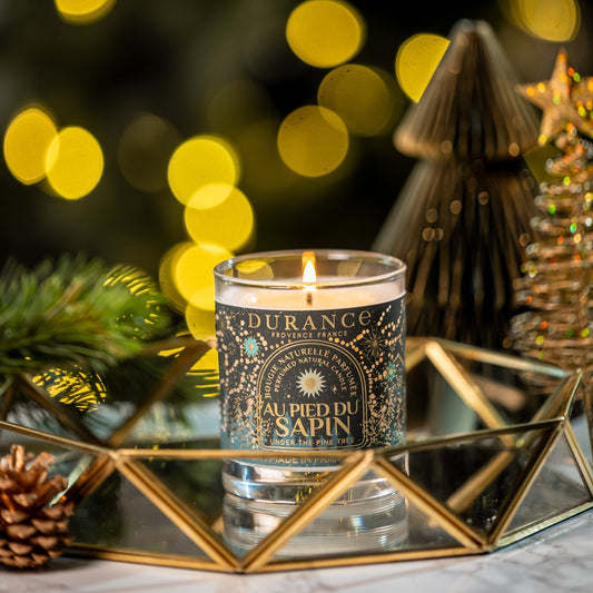 Candle in a decorative holder with blurred Christmas lights and tree in the background
