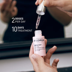 Person holding a Filorga skincare bottle with a dropper above it, against a blurred background.