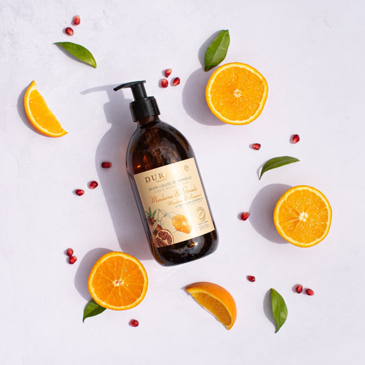 Brown bottle with pump dispenser labeled 'DURANCE' surrounded by sliced oranges and leaves on a light background