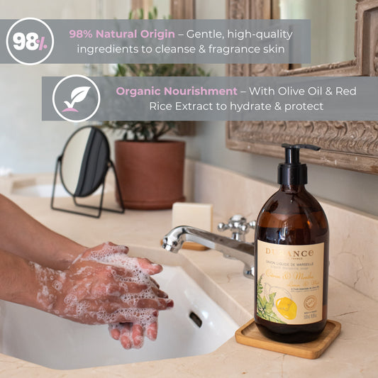 Person washing hands with a bottle of olive oil-based skincare product on a bathroom counter.