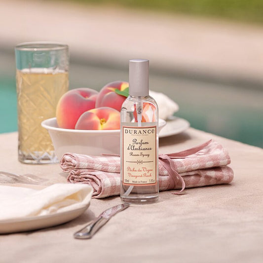 Bottle of Durance perfume on a table with peaches and a glass of juice.