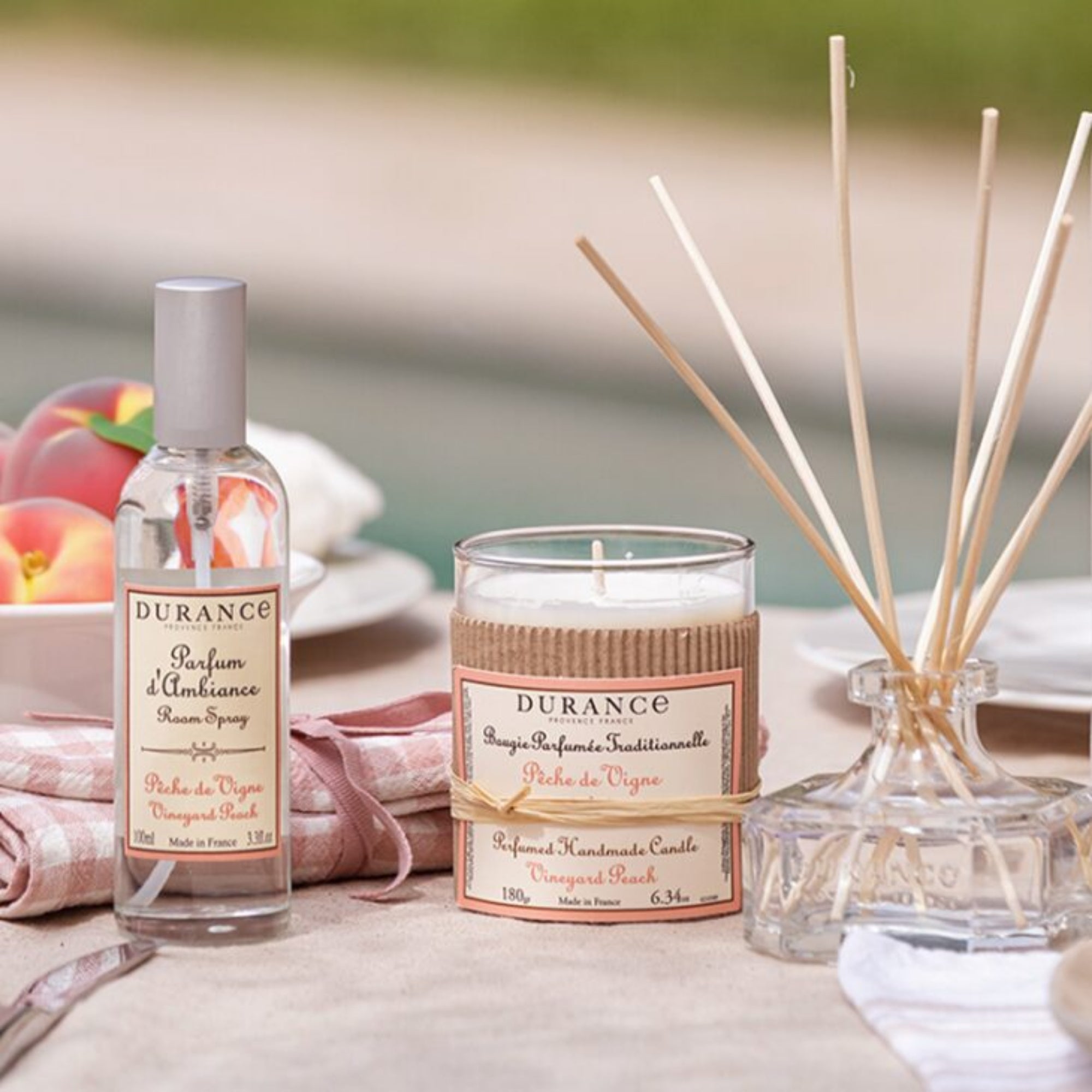 Durance perfume, candle, and diffuser on a table with peaches in the background