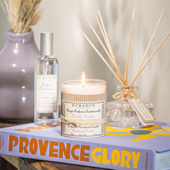Candle, bottle, and diffuser on a book titled 'Provence Glory' with decorative elements.
