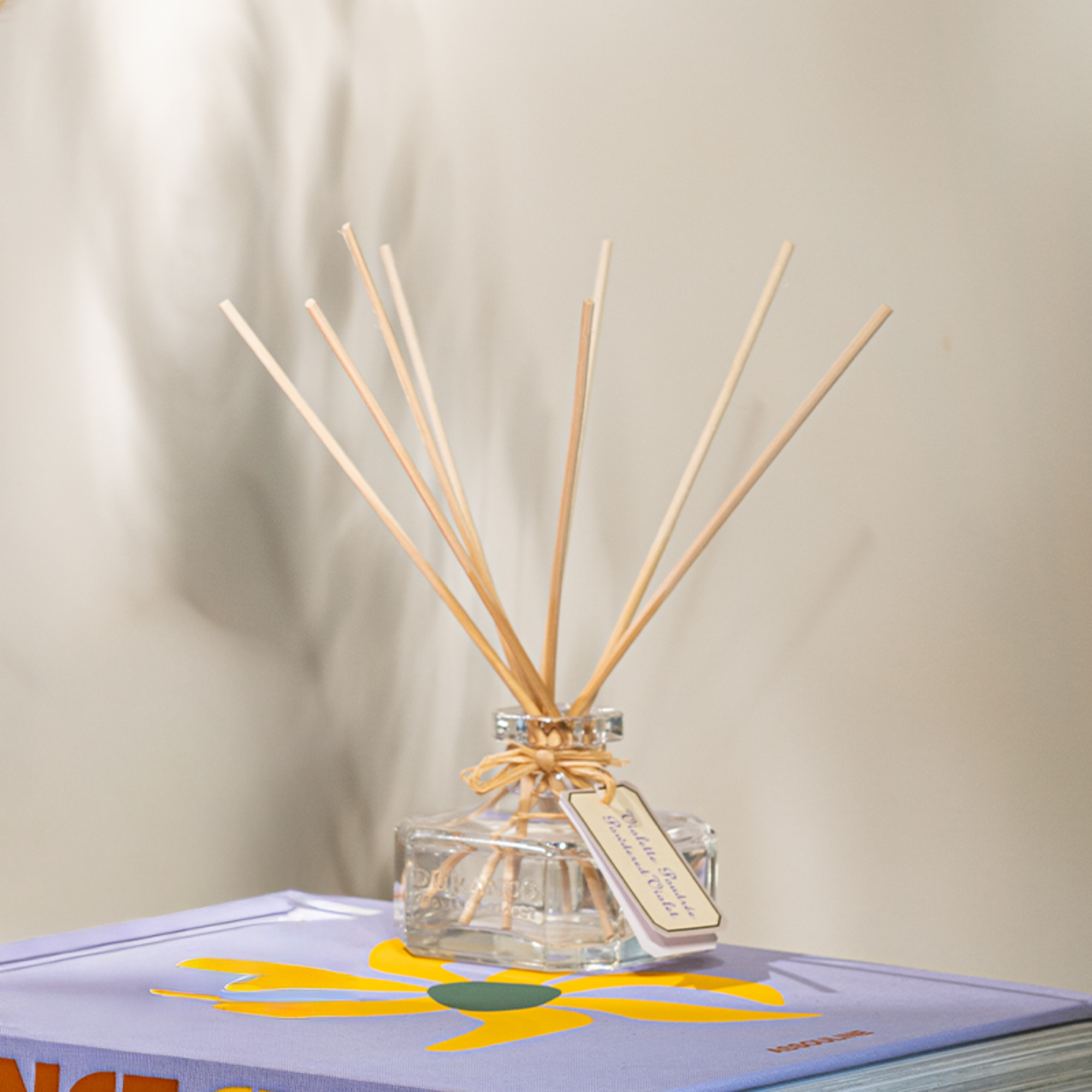 Reed diffuser with wooden sticks in a clear bottle on a book with a floral design.