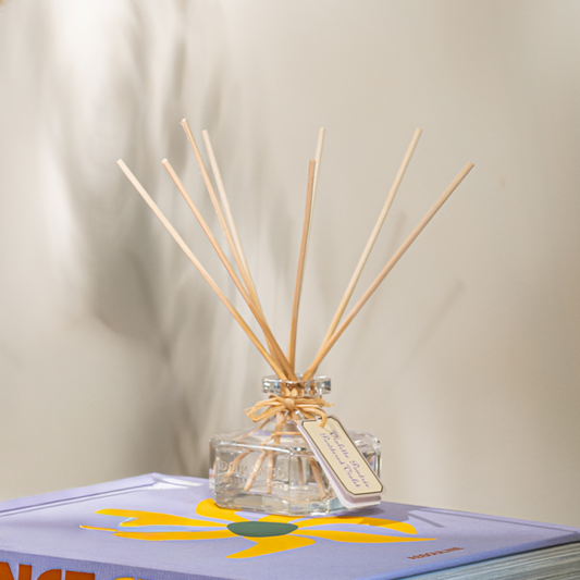 Reed diffuser with wooden sticks in a clear bottle on a book with a floral design.
